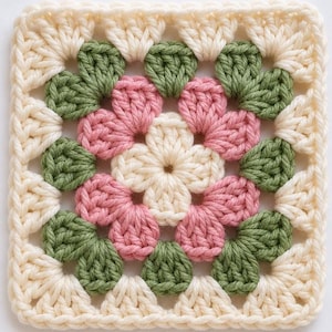 May include: A square crochet granny square featuring a central cream-colored flower motif surrounded by alternating clusters of sage green and dusty pink yarn. The outer border is finished with a cream-colored yarn in a classic crochet stitch pattern.