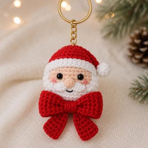 Può includere: Un portachiavi all'uncinetto a forma di Babbo Natale con un cappello rosso e bianco, un viso color pesca con occhi a perla neri, una barba bianca e un grande papillon rosso alla base. Fissato a un anello e una catena in metallo dorato.
