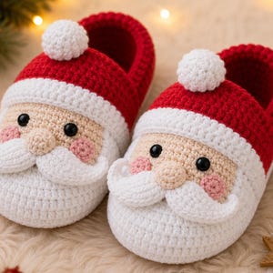 Könnte beinhalten: Ein Paar gehäkelte Hausschuhe im Design von Weihnachtsmann-Gesichtern. Die Hausschuhe haben eine rote Oberseite, einen weißen Rand, einen weißen Bommel oben sowie ein beiges Gesicht mit schwarzen Augen, rosa Wangen und weißem Bart.
