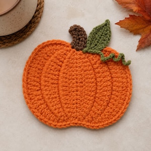 May include: A pumpkin-shaped crochet coaster made of orange yarn, featuring a brown stem and a green leaf with a curly vine detail. The coaster is crafted with visible stitches and has a rounded, ribbed texture resembling a real pumpkin.