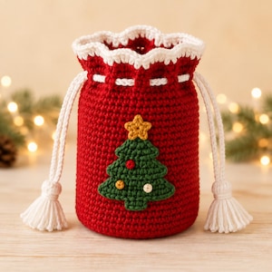 Può includere: Una pochette con coulisse in uncinetto rosso, caratterizzata da un bordo superiore smerlato bianco e cordini intrecciati bianchi con nappe. Il davanti presenta un'applicazione a forma di albero di Natale verde con una stella gialla e puntini.