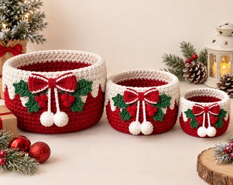 May include: Three round, crocheted storage baskets in descending sizes, featuring a deep red base and a cream-colored top rim. Each basket is decorated with a red bow, green holly leaves, red berries, and two white pom-poms hanging from strings.