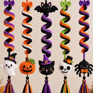 Può includere: Cinque ornamenti all'uncinetto da appendere con motivi a spirale in arancione, viola, nero, bianco e verde. Gli ornamenti includono un fantasma, una zucca, un gatto, un teschio e un ragno, ciascuno con un piccolo fiocco e una nappa in filo.