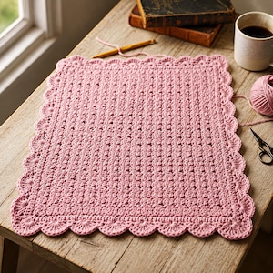 May include: A rectangular, dusty pink crocheted mat featuring a textured, repeating stitch pattern throughout the centre and a decorative, scalloped edge border that frames the entire piece, creating a soft and uniform appearance.