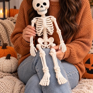 Pode incluir: Um boneco esqueleto de crochê na cor creme com um crânio detalhado com órbitas pretas, caixa torácica, braços articulados e pernas com articulações definidas. A figura de fio feita à mão apresenta pontos visíveis e uma textura.