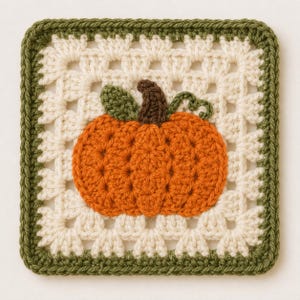 May include: A square crochet granny square featuring an off-white center with a textured orange pumpkin appliqué in the middle. The pumpkin has a dark brown stem and a green leaf and vine. The square is bordered by a dark olive green crochet edge.