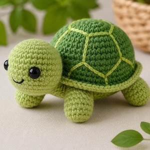 Op de afbeelding: Een kleine, handgemaakte gehaakte schildpad met een lichtgroene kop en ledematen, een donkergroen schild met lichtgroene stikdetails, twee ronde, zwarte plastic veiligheidsogen en een kleine, geborduurde zwarte mond op het gezicht.
