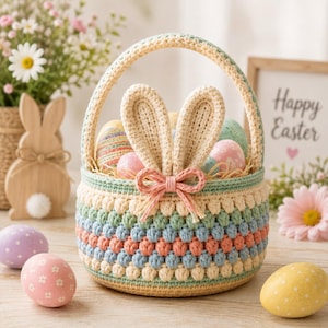 May include: A round crochet basket featuring a pastel color palette of cream, light blue, and peach with a textured bobble stitch pattern. The basket has a sturdy handle and two upright crochet bunny ears attached to the front with a small pink bow.
