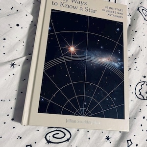 Puede incluir: Un libro de tapa dura titulado "Forty Ways to Know a Star" con una cubierta azul oscuro que presenta un mapa estelar y una imagen de galaxia. El libro está sobre una superficie blanca estampada. También se ve el texto "Using Stars to Understand Astronomy".