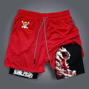 Puede incluir: Pantalones cortos deportivos rojos con cintura con cordón y una capa interior negra. Los pantalones cortos presentan un logotipo blanco de calavera y huesos cruzados con un sombrero de paja en la parte delantera y una impresión gráfica en la capa interior.