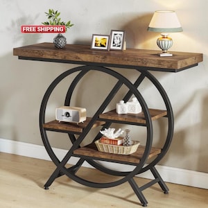 Könnte beinhalten: Eine braune und schwarze Konsolentisch mit einem einzigartigen kreisförmigen Design. Der Tisch hat eine rechteckige Oberseite und drei Regale. Dekorative Gegenstände sind eine Lampe, ein kleines Radio und gerahmte Fotos. Der Tisch ist 122 cm lang.