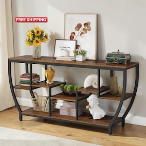 May include: A brown and black console table with multiple shelves. The table has a metal frame and a wooden top. Decorative items include a vase of sunflowers, books, and a white bust.