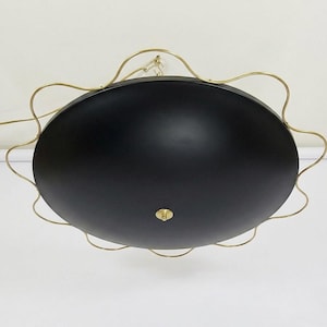 May include: A black, oval-shaped ceiling light fixture with a gold-colored, wavy metal frame. The light has a matte finish and a small, gold-colored central detail. The fixture is suspended from the ceiling.