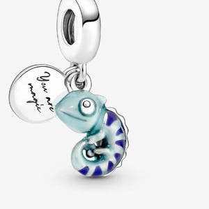 Può includere: Un charm in argento con un design di camaleonte azzurro e un piccolo charm rotondo con la scritta "You are magic". Il camaleonte ha strisce blu scuro e una coda arricciata. Il charm ha un anello d'argento nella parte superiore.