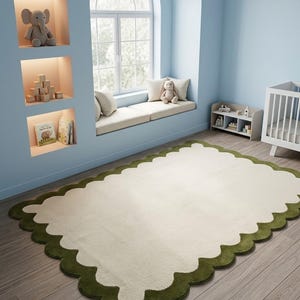 Puede incluir: Una alfombra rectangular con un centro color crema y un borde festoneado verde oscuro. La alfombra est&aacute; colocada sobre un suelo de madera clara en una habitaci&oacute;n con paredes azules, un asiento junto a la ventana y una cuna, lo que sugiere una habitaci&oacute;n infantil.