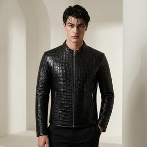 Peut inclure: Une veste noire avec un motif texturé en peau de crocodile, un col montant et une fermeture éclair frontale intégrale. Le vêtement comprend deux poches latérales avec des fermetures éclair argentées, des manches longues et une coupe ajustée.
