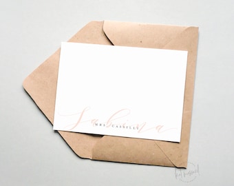 May include: A white card with a pink cursive script that says "Sabrina" and "Mrs. Cassili" in black text. The card is in a brown envelope.