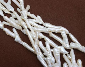 Könnte beinhalten: Nahaufnahme einer Sammlung weißer, unregelmäßig geformter Perlen. Die Perlen haben einen glänzenden, perlmuttartigen Glanz und sind vor einem braunen Hintergrund angeordnet. Die organischen Formen der Perlen deuten auf einen natürlichen Ursprung hin, möglicherweise für Schmuck.