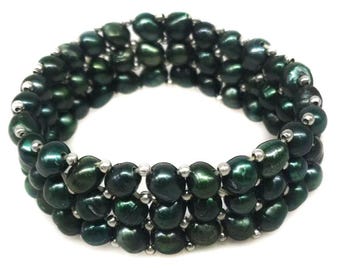 Könnte beinhalten: Ein mehrreihiges Armband mit drei Reihen dunkelgrüner, unregelmäßig geformter Süßwasserperlen. Die Perlen sind mit kleinen, runden, silberfarbenen Metallperlen aufgereiht, die zwischen jeder Perle liegen und ein geschichtetes Design bilden.