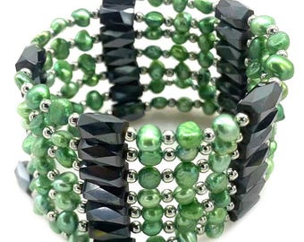 Könnte beinhalten: Ein mehrreihiges Armband mit der Aufschrift No. 33, bestehend aus Reihen kleiner, glänzender grüner Perlen, durchsetzt mit winzigen silberfarbenen Kügelchen und vertikalen Säulen aus facettierten, dunkel anthrazitfarbenen Steinen.