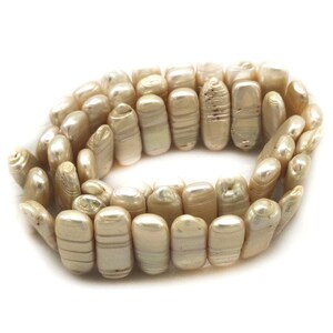Op de afbeelding: Een ketting van crèmekleurige barokparels. De parels hebben een glanzende glans en variëren in grootte en vorm, sommige vertonen natuurlijke ribbels. De ketting is in een cirkelvormig patroon gerangschikt en toont de unieke textuur van elke parel.