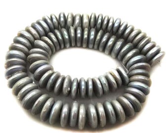 Könnte beinhalten: Ein Strang aus kreisförmigen, münzförmigen Perlen mit einer glatten, irisierenden grauen Oberfläche. Die Perlen sind in einer lockeren, überlappenden Spirale angeordnet und zeigen ihre einheitliche Größe und ihren metallischen Glanz.