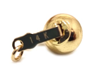 Könnte beinhalten: Ein goldener Kugelanhänger mit einem kleinen, dunklen, rechteckigen Schildchen an der Oberseite. Auf dem Schildchen ist deutlich die Gravur 14 K zu sehen, die den Goldgehalt angibt. Ein kleiner, runder Biegering ist am Ende des Schildchens befestigt.