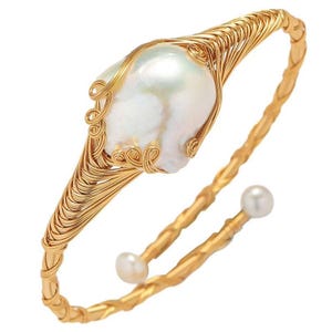May include: A gold-toned cuff bracelet featuring a large, irregular white pearl at its center. The pearl is cradled by intricate wirework. Two smaller pearls adorn the open ends of the bracelet, adding to its elegant design. The bracelet has a twisted rope design.