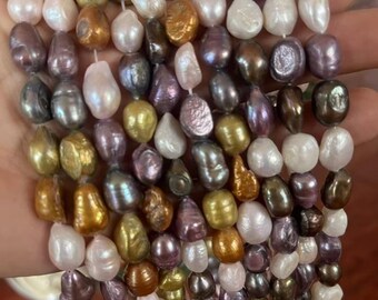 Könnte beinhalten: Eine Sammlung mehrfarbiger Barockperlen, die auf dünne weiße Fäden aufgezogen sind. Die Perlen haben unregelmäßige, organische Formen und eine glänzende Oberfläche in den Farben Weiß, Creme, Gold, Bronze, Lavendel, Violett und Dunkelgrau.