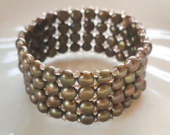Könnte beinhalten: Ein breites Armband aus mehreren Reihen runder, metallisch olivgrüner Perlen. Die Perlen sind in einem strukturierten, gitterartigen Muster angeordnet und durch kleine, klare, transparente Zwischenperlen im gesamten Design miteinander verbunden.