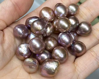 Könnte beinhalten: Eine Sammlung glänzender, unregelmäßig geformter Perlen in den Farbtönen Lavendel, Bronze und Gold. Die Perlen haben eine glatte, schillernde Oberfläche, die das Licht reflektiert. Diese Naturperlen sind eine schöne Ergänzung zu Schmuck.