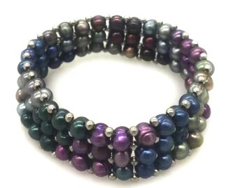 Könnte beinhalten: Ein mehrreihiges Armband bestehend aus drei Reihen kleiner, irisierender Süßwasserperlen in den Farben Dunkelviolett, Dunkelblau, Waldgrün und Anthrazit, die durch winzige silberfarbene Metallperlen im gesamten kreisförmigen Design getrennt sind.