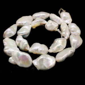 Op de afbeelding: Een ketting van witte barokparels. De parels hebben onregelmatige vormen en een iriserende glans met hints van roze, groen en geel. Ze zijn geregen op een draad, wat een elegant sieraad creëert.
