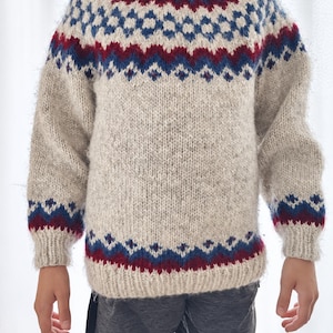 Può includere: Un maglione a maniche lunghe con girocollo in color avena chiaro, caratterizzato da una lavorazione a maglia soffice e testurizzata. Lo sprone e i polsini presentano un motivo geometrico ripetuto in blu profondo e rosso scuro, con bordi a coste.
