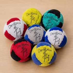 May include: A collection of seven multi-colored fabric footbags, each featuring the text DIRT BAG and a stick figure graphic. The balls are rendered in various color combinations including red and white, yellow, teal and black, blue and gray, and blue and yellow.