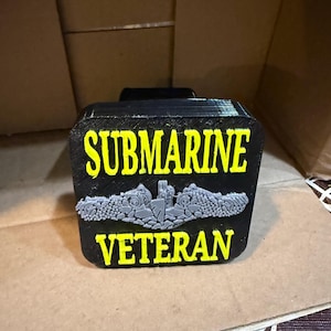May include: Black rectangular plaque with yellow text reading "SUBMARINE VETERAN." A gray emblem of a submarine and related imagery is centered below the word "SUBMARINE." The plaque is likely a commemorative item.