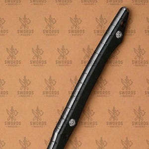 May include: A black sword handle with silver accents and rivets. The handle is long and slender, with a textured grip. The background features a repeating pattern of crossed swords and axes with the text "SWORDS -MAKERS-".