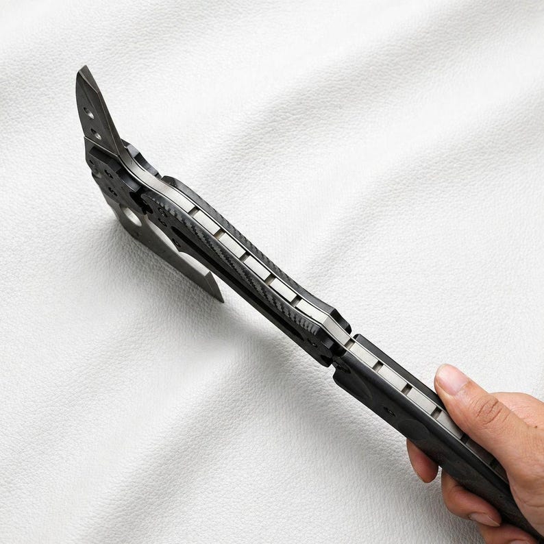 May include: A black and silver tactical tomahawk axe with a sharp blade and a textured handle. The axe features a hammer head and a pointed spike, ideal for outdoor activities and survival.