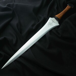 May include: A silver dagger with a pointed blade and a wooden handle. The handle has a textured, brown appearance. The blade features an etched design near the handle. The dagger is displayed against a black background.