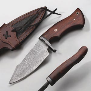 May include: A hunting knife with a patterned steel blade and a dark wood handle. The knife is accompanied by a brown leather sheath. The handle has a small decorative inlay. The blade has a unique pattern.