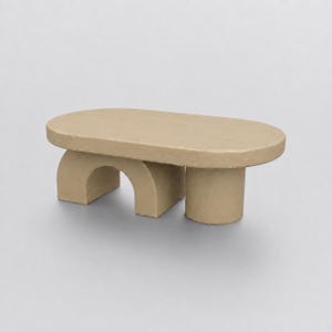 May include: A low, oval-shaped coffee table with a smooth, matte beige finish. The table features a unique base design consisting of one arched, semi-circular support on the left side and a single cylindrical pillar support on the right side.