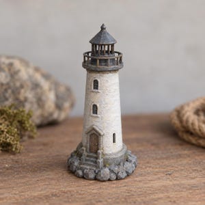 May include: A miniature lighthouse figurine featuring a weathered white cylindrical tower, a dark gray conical roof, and a small lantern room. The structure sits on a base of textured gray rocks and includes a brown door with stone steps.