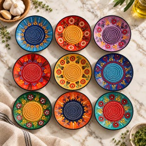 Peut inclure: Neuf râpes en céramique circulaires disposées en grille, chacune présentant une surface de râpage texturée centrale entourée de motifs floraux et de tulipes peints à la main dans des tons de bleu, rouge, jaune, vert, violet et orange.