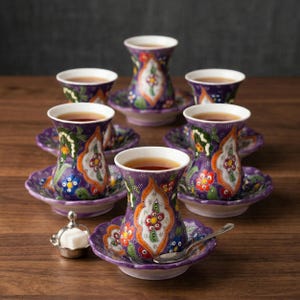 May include: A set of six purple Turkish tea glasses with matching saucers, filled with tea. The glasses and saucers are decorated with colorful floral patterns in orange, green, and blue. A small silver sugar bowl and spoon are also present.