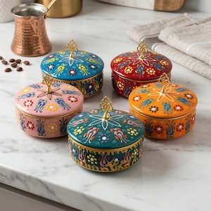 May include: Five colorful, round ceramic jars with lids, each adorned with intricate floral and bird patterns. The jars are in shades of blue, red, orange, pink, and teal, with gold accents and ornate handles. These decorative jars are ideal for storing small items.