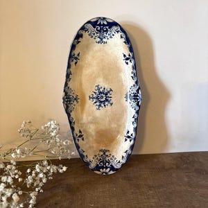 Könnte beinhalten: Eine ovale Servierplatte aus Keramik mit cremefarbener Mitte, gesprenkelter Textur und dunkelblauem Zierrand. Der Rand ist mit komplexen blauen Blumen- und Schnörkelmustern verziert, in der Mitte befindet sich ein passendes blaues Blumenmotiv.