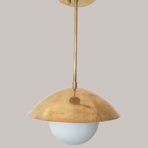 Puede incluir: Una l&aacute;mpara colgante dorada con una pantalla redondeada y un globo blanco. La l&aacute;mpara tiene un soporte circular para el techo y una varilla delgada. La pantalla es de color dorado c&aacute;lido y el globo es blanco suave. El dise&ntilde;o general es moderno y minimalista.