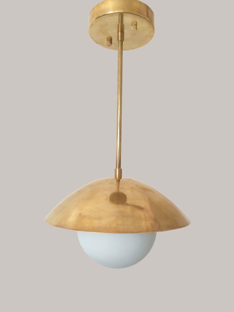 Puede incluir: Una l&aacute;mpara colgante dorada con una pantalla redondeada y un globo blanco. La l&aacute;mpara tiene un soporte circular para el techo y una varilla delgada. La pantalla es de color dorado c&aacute;lido y el globo es blanco suave. El dise&ntilde;o general es moderno y minimalista.