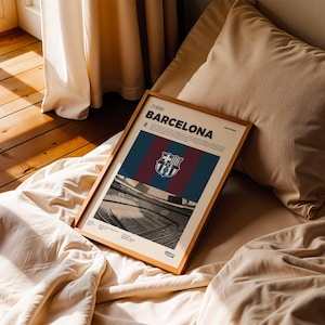 May include: A framed poster featuring the FC Barcelona logo and team colors of blue, maroon, and red. The poster includes the text "/1899 BARCELONA" and a black and white image of a stadium. The frame is made of wood.