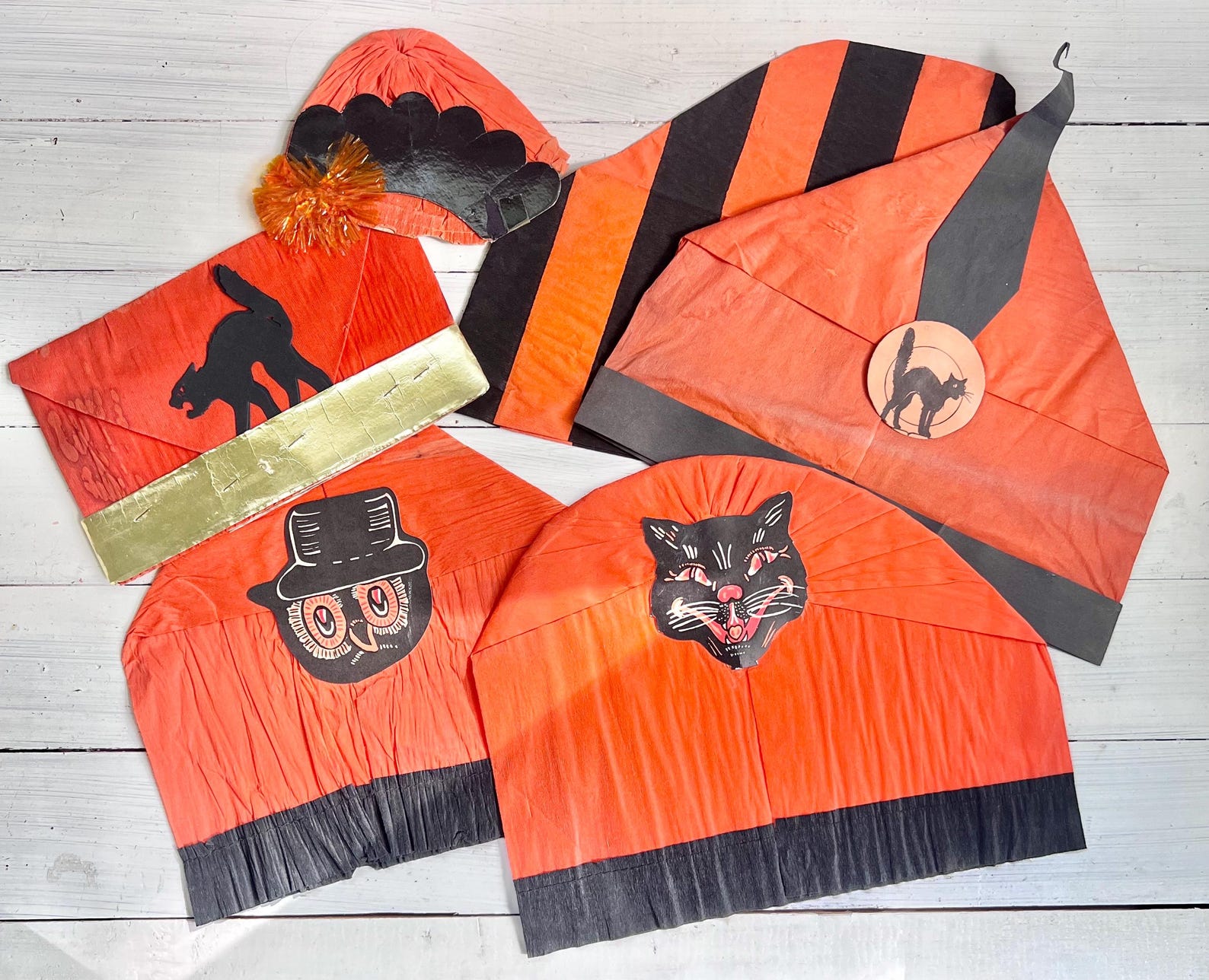 A Flat-Top Vintage Party Crown Vintage orange-and-black paper Halloween hats with broad folded bands and printed motifs.